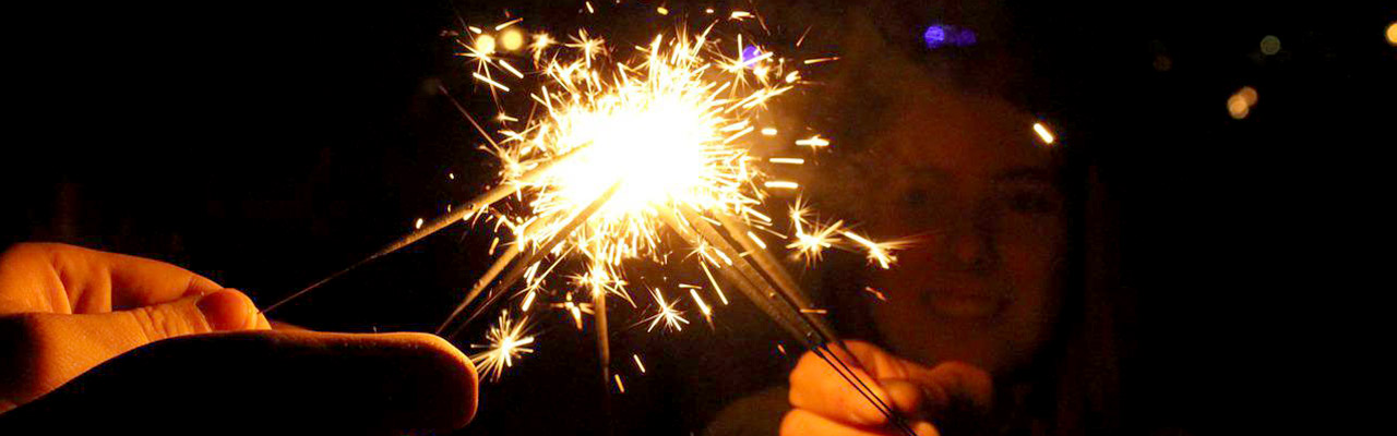 Several people holding lit sparklers up together at a point.